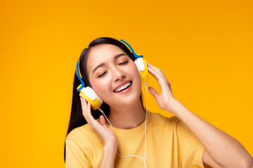 Beautiful asian woman listening music in headphones with smile face. She singing song on yellow background. Charming girl get happy and enjoy listening song. Attractive lady enjoying life. copy space