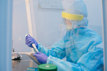 A scientist in PPE safty uniform pipetting sample experiment in biological safety cabinet (BSC).