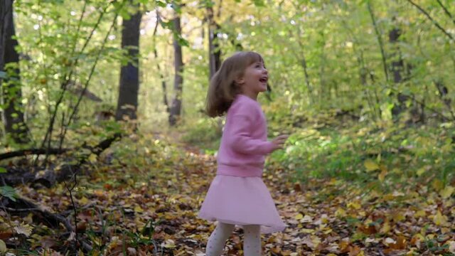 A cheerful girl spins and rejoices when fallen autumn leaves fall on her