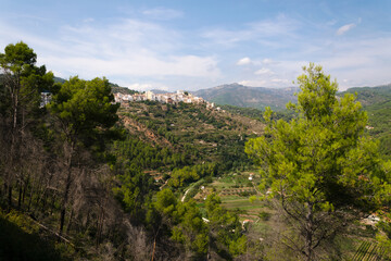 Among the trees a view of the village Lucena del Cid surrounded by nature on a day with blue sky and clouds, Castellon, Spain