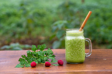 Green smoothie of parsley, avocado, honey and banana in a glass mug on a wooden table in a garden cafe, close-up