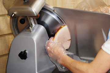 The chef slices the ham with an electric slicer.