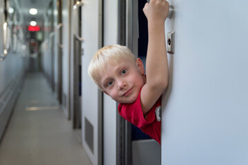 Blond boy in train carriage looks out of compartment. Traveling with children by train.