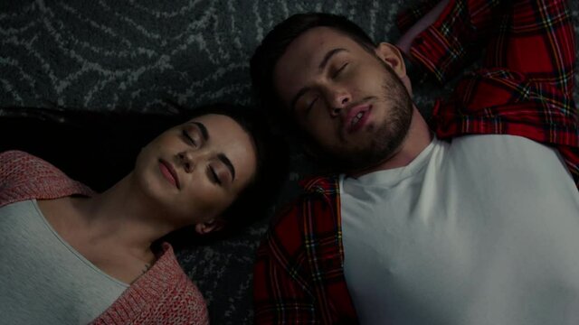 Young man and woman are lying on a floor at home, have closed their eyes, relaxing and communicating after hard working day, have nice time together, Foreground, Slow motion.