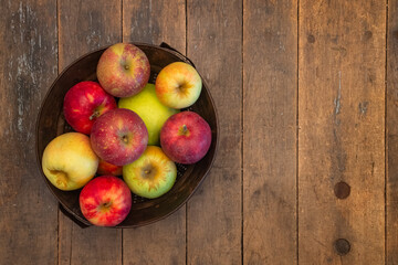 several varieties of fresh picked apples in a colander sitting on a farm table