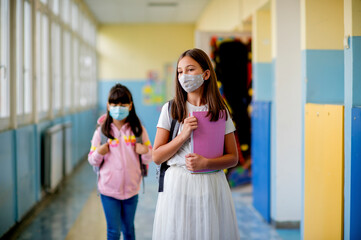Elementary school students walking down the hallway in between classes. They wearing protective...