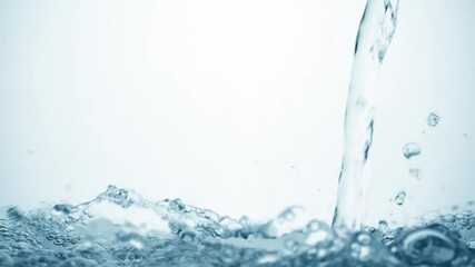 Freshness of a clear blue liquid on white background. Brilliant stream of water in slow motion falls on smooth clean surface, creating air bubbles, drop splashes and ripples after falling, side view
