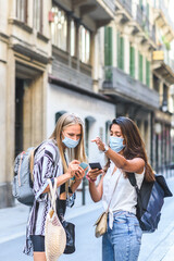 young indian woman pointing direction in the street to a caucasian blonde woman and looking to phone