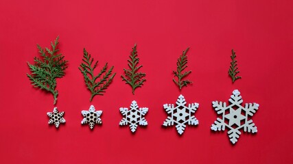 Fototapeta na wymiar Abstract composition of decorative snowflakes and Christmas tree branches on a red background. Christmastime.