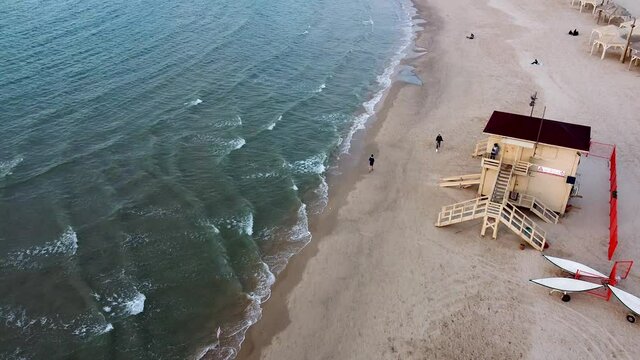 Aerial long shot follow man running at the beach, lifeguard stand, drone shot