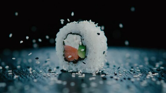 Rol de Sushi en tabla negra con lluvia de ajonjol&iacute;, lluvia de semillas de s&eacute;samo.  240 fps HD.