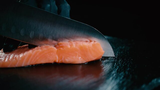 Chef de Sushi cortando un pedazo de salm&oacute;n con cuchillo afilado en una tabla negra. HD