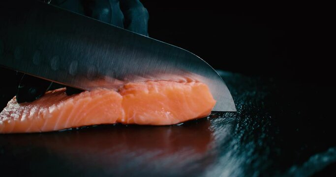 Chef de Sushi cortando pedazo de salm&oacute;n con cuchillo afilado sobre una tabla negra. 4K