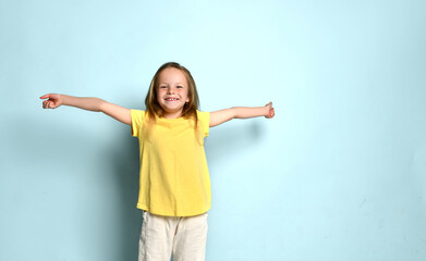 Little female in yellow t-shirt and white pants. She spreading her hands wide apart and screaming, posing on turquoise background. Close up