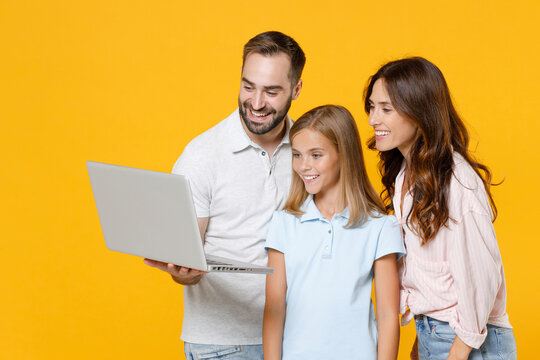 Smiling Funny Young Parents Mom Dad With Child Kid Daughter Teen Girl In Basic T-shirts Using Laptop Pc Computer Isolated On Yellow Background Studio Portrait. Family Day Parenthood Childhood Concept.