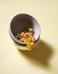 a cluster of juicy green pink grapes in a gray bowl  on a yellow background