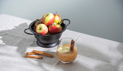 a glass of freshly brewed apple drink with apple slices and cinnamon on linen tablecloth