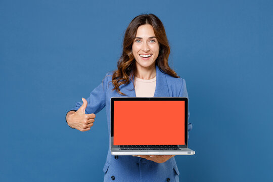 Smiling young brunette woman 20s wearing basic jacket hold laptop pc computer with blank empty screen mock up copy space showing thumb up isolated on bright blue colour background studio portrait.