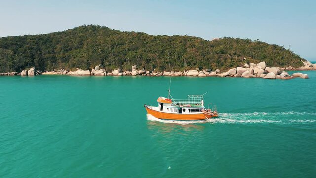 Cinematic aerial shot of a tourist boat passing by on turquoise water color and brazilian paradisiac rainforest beach scenery sea