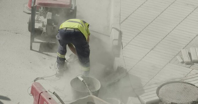 Construction worker cutting a cement tile into a lot of dust on city street
