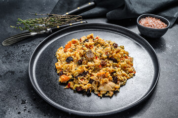 Obraz na płótnie Canvas Rice pilaf with lamb meat and vegetables in a plate. Black background. Top view