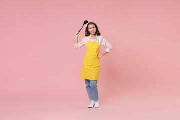 Full length portrait of preoccupied puzzled young woman housewife in apron hold soup black ladle dipper while doing housework isolated on pastel pink colour background studio. Housekeeping concept.