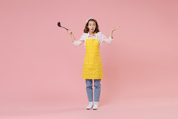 Full length portrait shocked young woman housewife in apron hold soup black ladle dipper spreading hands while doing housework isolated on pastel pink colour background studio. Housekeeping concept.