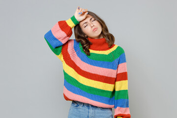 Exhausted tired sick dissatisfied young brunette woman 20s wearing casual colorful knitted sweater standing put hand on head keeping eyes closed isolated on grey colour background, studio portrait.