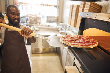 Cheerful young man enjoying work in pizzeria