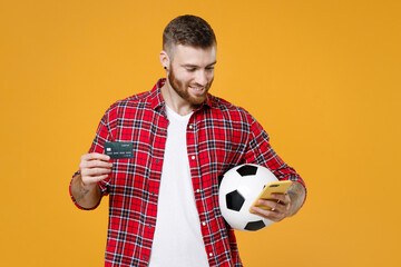 Smiling young man football fan in red shirt cheer up support favorite team with soccer ball using...