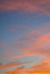 Crescent Moon with a blue sky and sunset colored clouds 