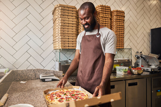 Cheerful young man standing at the counter with pizza