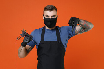 Dissatisfied professional tattooer master artist tattooed man in apron face mask hold machine black...