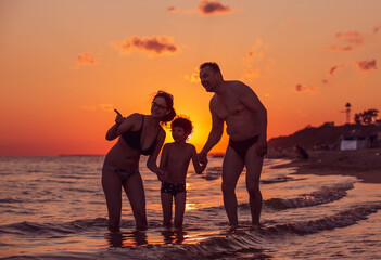 Dark silhouette of a happy family on a sunset.Father, mother, baby son walking along the sandy beach.Family having fun on the beach.Travel lifestyle, parents, dad with children on summer vacation.