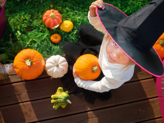 Girl in witch costume sitting with pumpkins on wooden terrace
