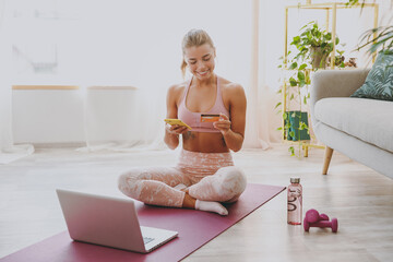 Smiling young strong sporty fitness woman wearing pink tracksuit doing yoga exercises using laptop...