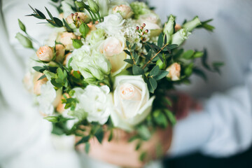 Bridal bouquet, hold the wedding bouquet in your hand, satin ribbons adorn the wedding bouquet of roses, on the background of the bride's dress, fresh flowers, made by a florist