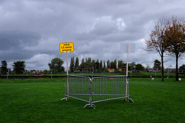 Translation: Keep 1.5 distance.  A yellow warning sign in the middle of a grass field of Amsterdams Wester Park. Hardly no one is outside on this cloudy cold autumn day.