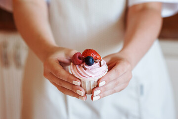 Woman holds creamy cupcake with fresh berries in her hands in front of the apron. Delicious homemade or restaurant dessert.