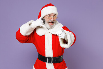 Fototapeta na wymiar Santa Claus man in Christmas hat red coat glasses doing phone gesture says call me back pointing index finger on camera isolated on violet background. Happy New Year celebration merry holiday concept.