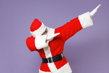 Santa Claus man in Christmas hat red suit coat doing dab hip hop dance hands gesture, youth sign hiding covering face isolated on violet background. Happy New Year celebration merry holiday concept.