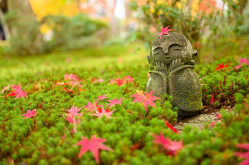 Red Maple leaf on head of Jizo sculpture doll (little Japanese Buddhist monk doll rock) in Japanese Garden