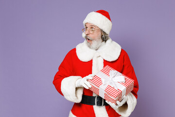 Shocked Santa Claus man in Christmas hat red suit coat gloves glasses hold present box with gift ribbon bow isolated on violet background studio. Happy New Year celebration merry holiday concept.