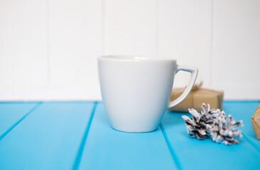 Mock up of white cup on the wooden table, place for a text. Presents and pines.