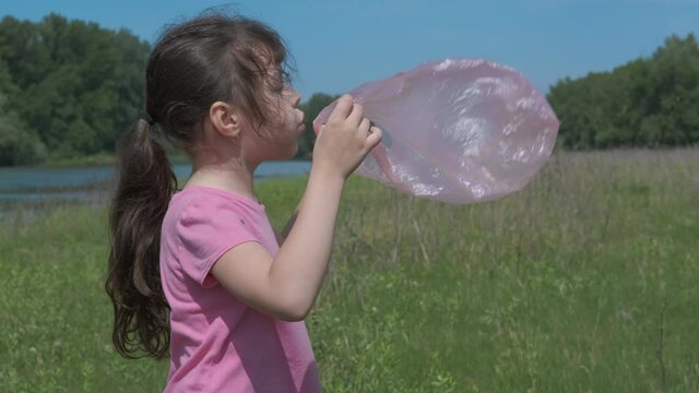 A child with a plastic bag. Little girl blows into a plastic bag outdoors.
