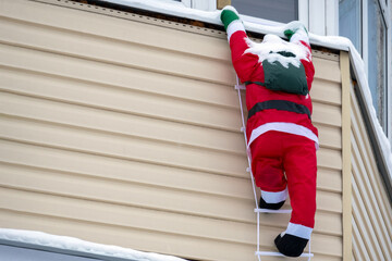 Christmas decor. Figure of decorative Santa Claus on the facade of the house. Santa Claus with a bag of gifts climbs the rope ladder. Copy space.