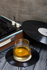 Old turntable. Nearby is a glass of strong alcohol. Retro party equipment.
