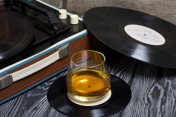 Old turntable. Nearby is a glass of strong alcohol. Retro party equipment.