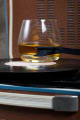 Old turntable. Nearby is a glass of strong alcohol. Retro party equipment.