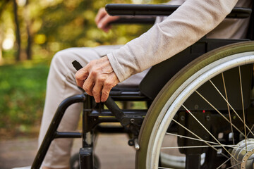 Obraz premium Wrinkled hand on a wheelchair handle outdoors